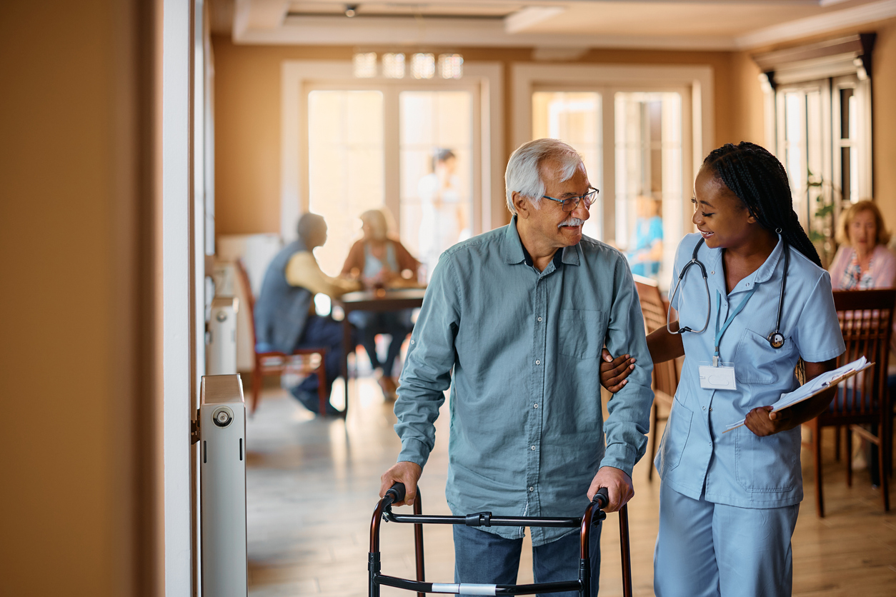 Nurse assisting senior man with walker in assisted living community, providing compassionate senior care guidance.