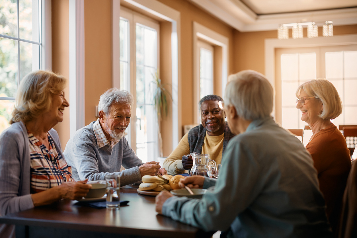 Group of seniors enjoying a meal together in an adult family home setting.