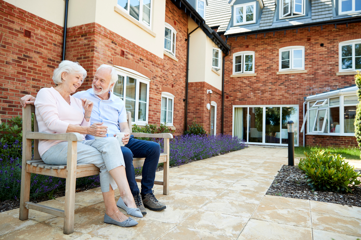 Senior couple relaxing on bench in independent living community setting.
