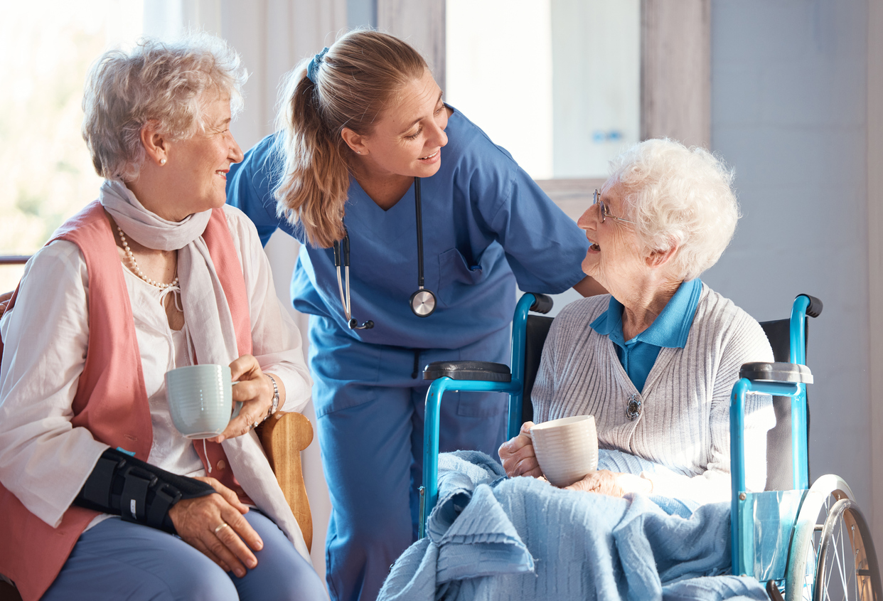 RN advisor assisting senior woman in wheelchair and seated woman with coffee, memory care community